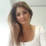 Freundliche Frau mit schulterlangen braunen Haaren, trägt ein weißes Top.