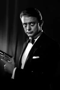 Schwarz-Weiß-Porträt eines Mannes im Smoking, der eine Pistole hält.